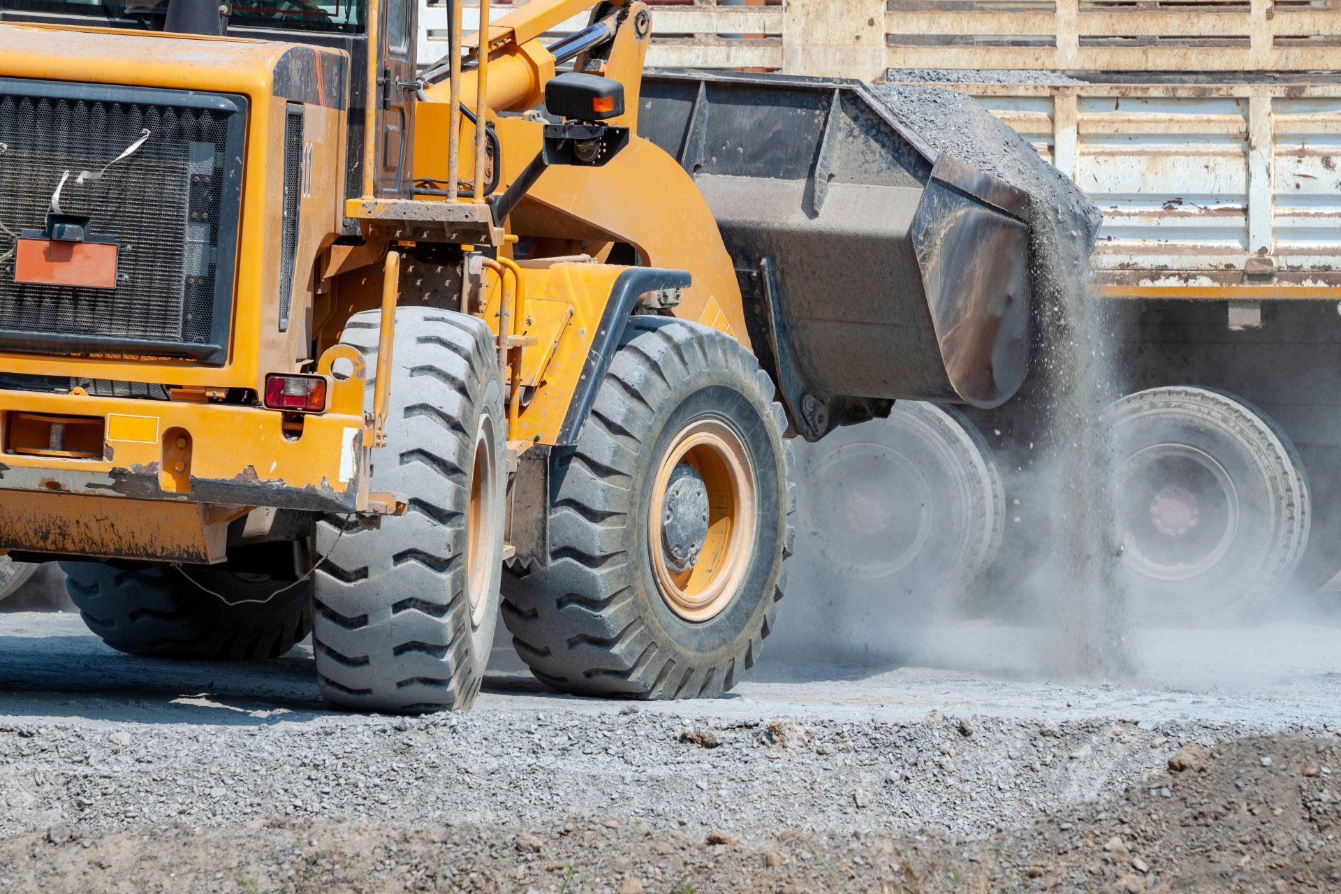 a yellow bulldozer is loading gravel into a truck