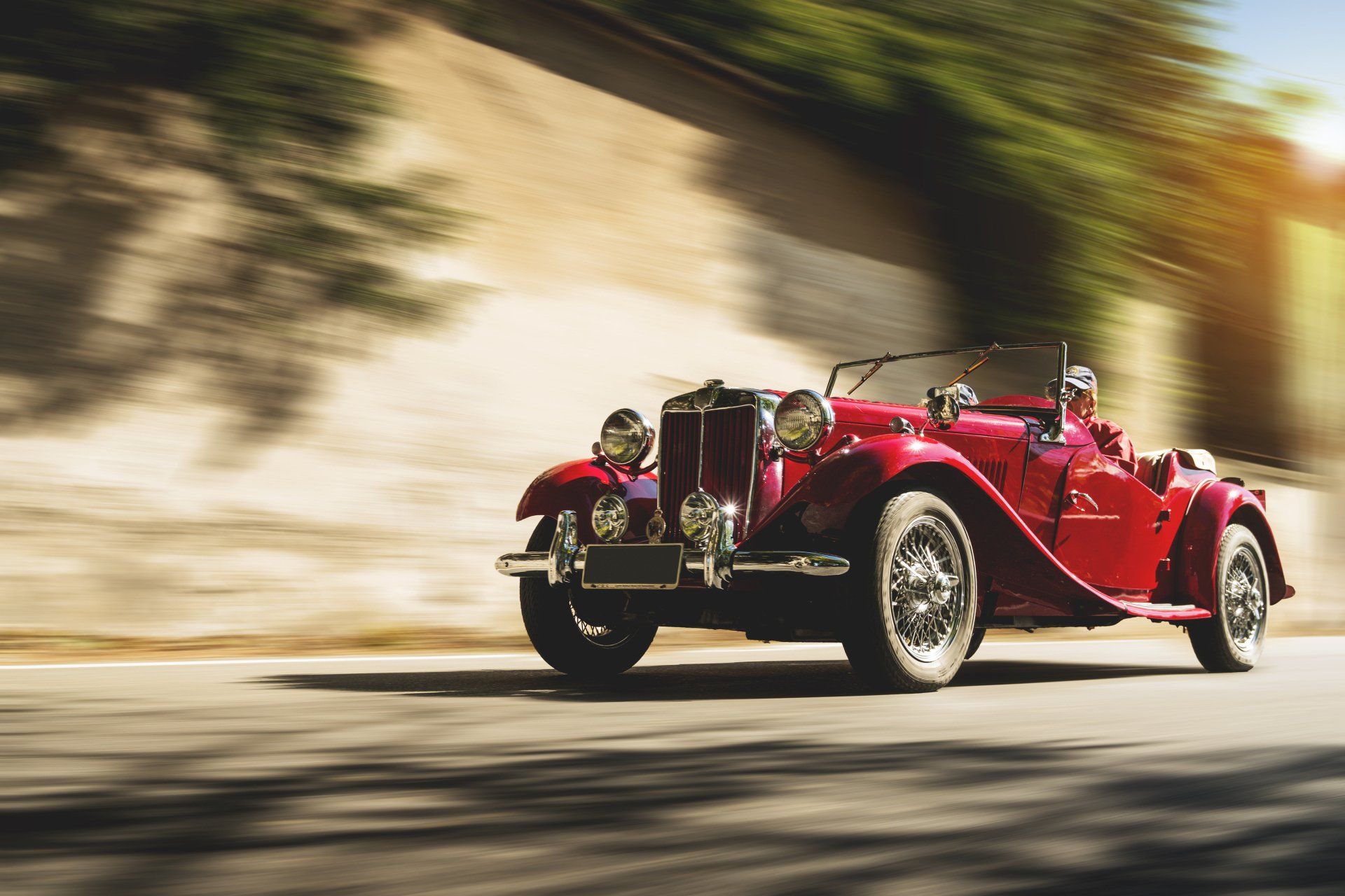 an old red car is driving down a road