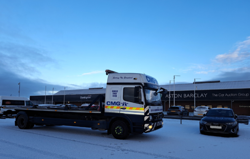 a cmg tow truck is parked in front of an aston barclay car auction group