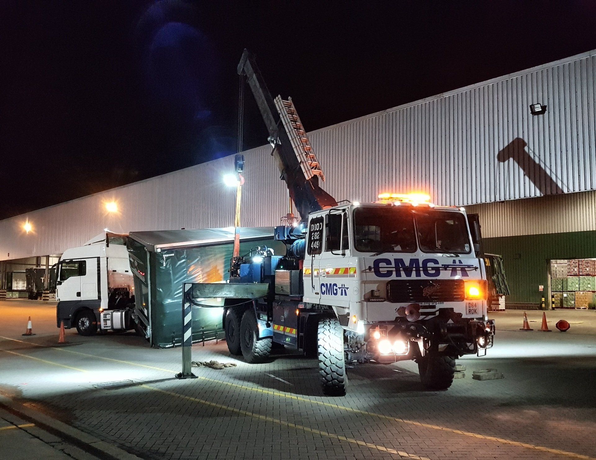 A truck with a crane attached to it is parked in front of a building at night.