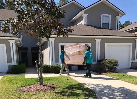 Two movers carrying rolled carpet, one giving a thumbs-up in a light-filled room. Two movers carrying rolled carpet, one giving a thumbs-up in a light-filled room.