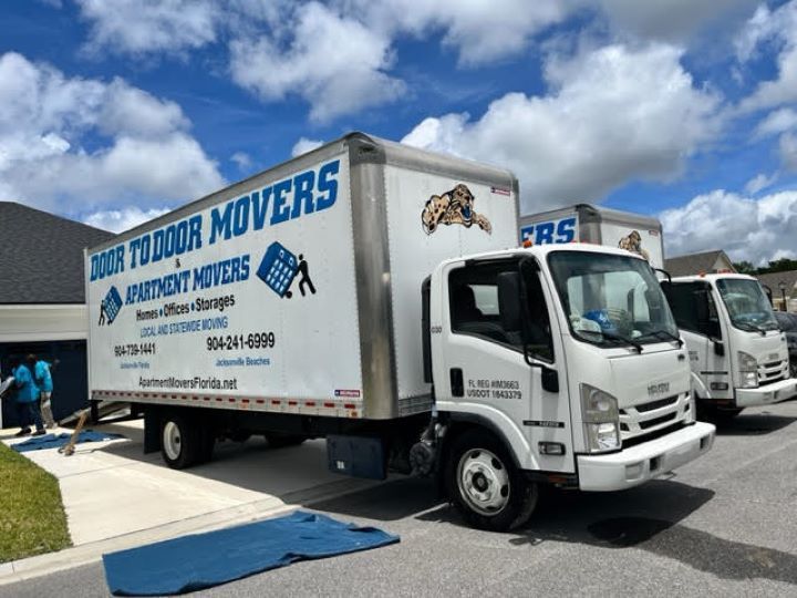 Moving trucks labeled Door to Door Movers parked in front of a house. Workers loading.