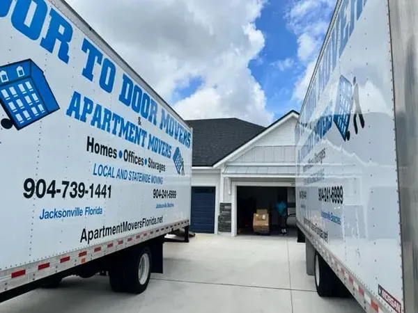 Two Door To Door Apartment Movers trucks parked in front of a house, one in the driveway, the other in the street.