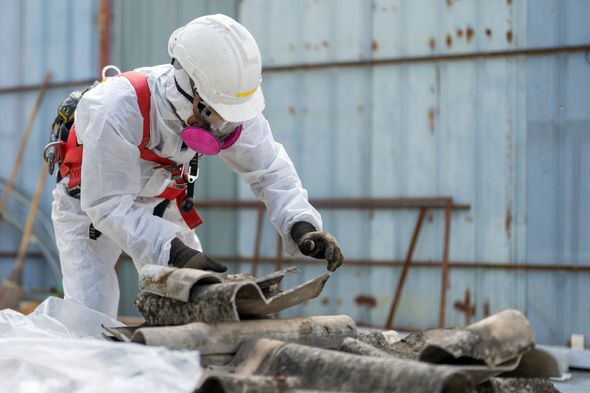 A man in a protective suit is working on a pile of asbestos.