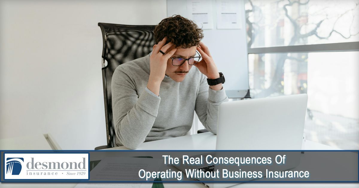 Man stressed at a laptop, likely due to the lack of business insurance. Indoor office setting.