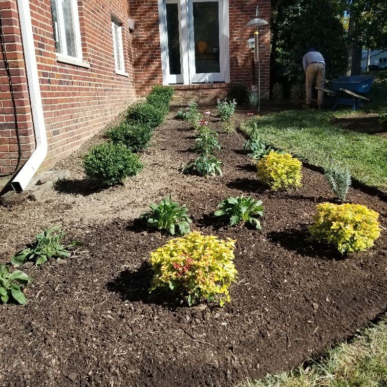 A man is working on a garden in front of a brick house