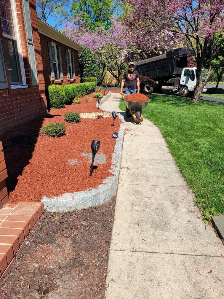 A man is pushing a wheelbarrow full of mulch down a sidewalk.