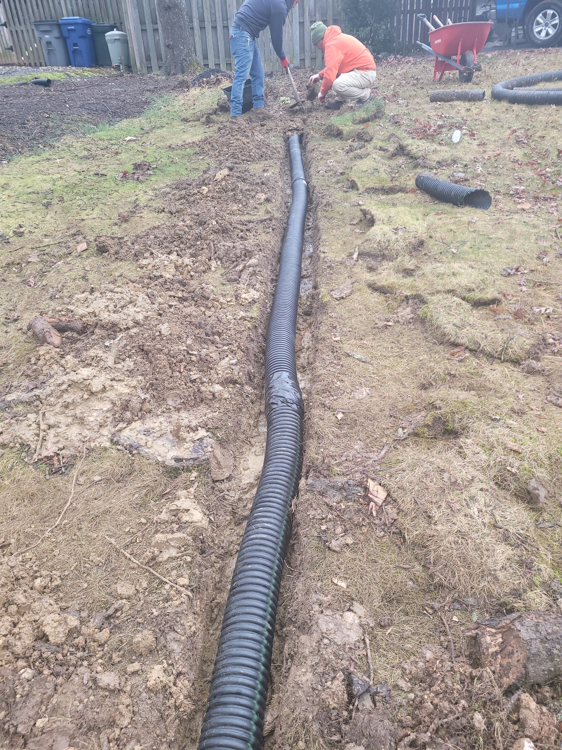 Two men are working on a drainage system in a yard.