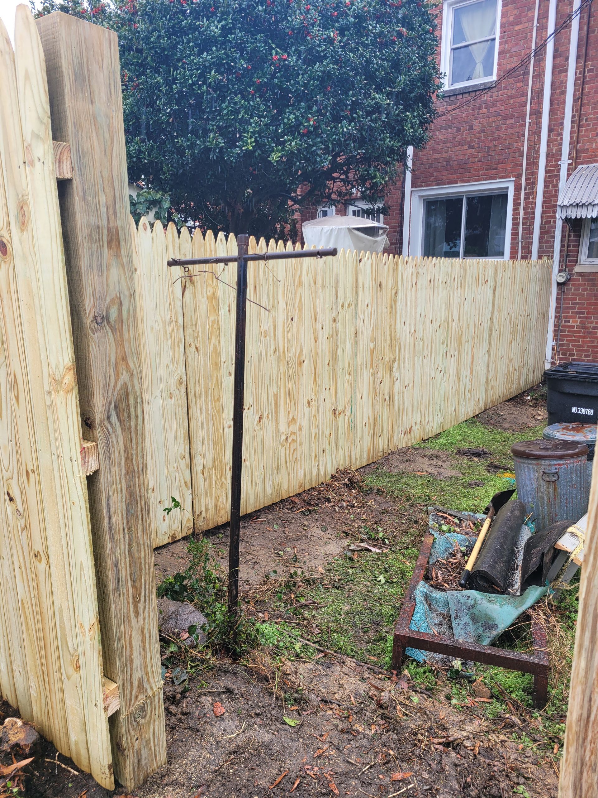 A wooden fence in a backyard with a brick building in the background.