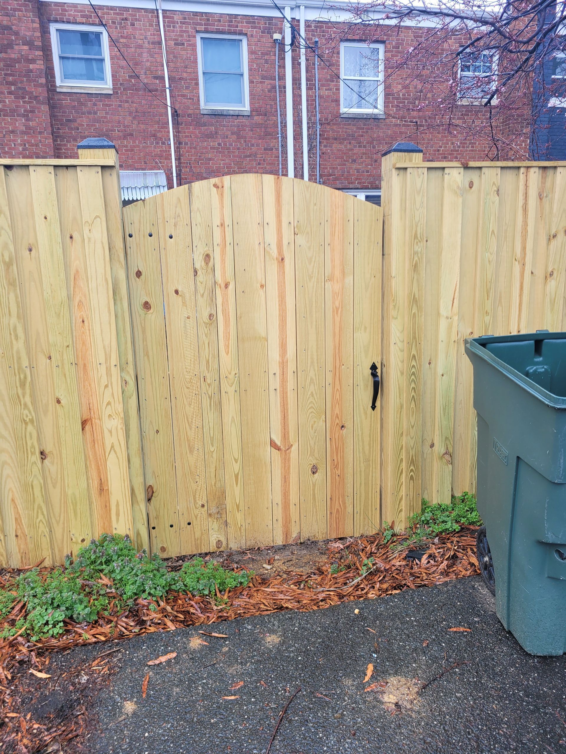 A wooden fence with a green trash can in front of it.