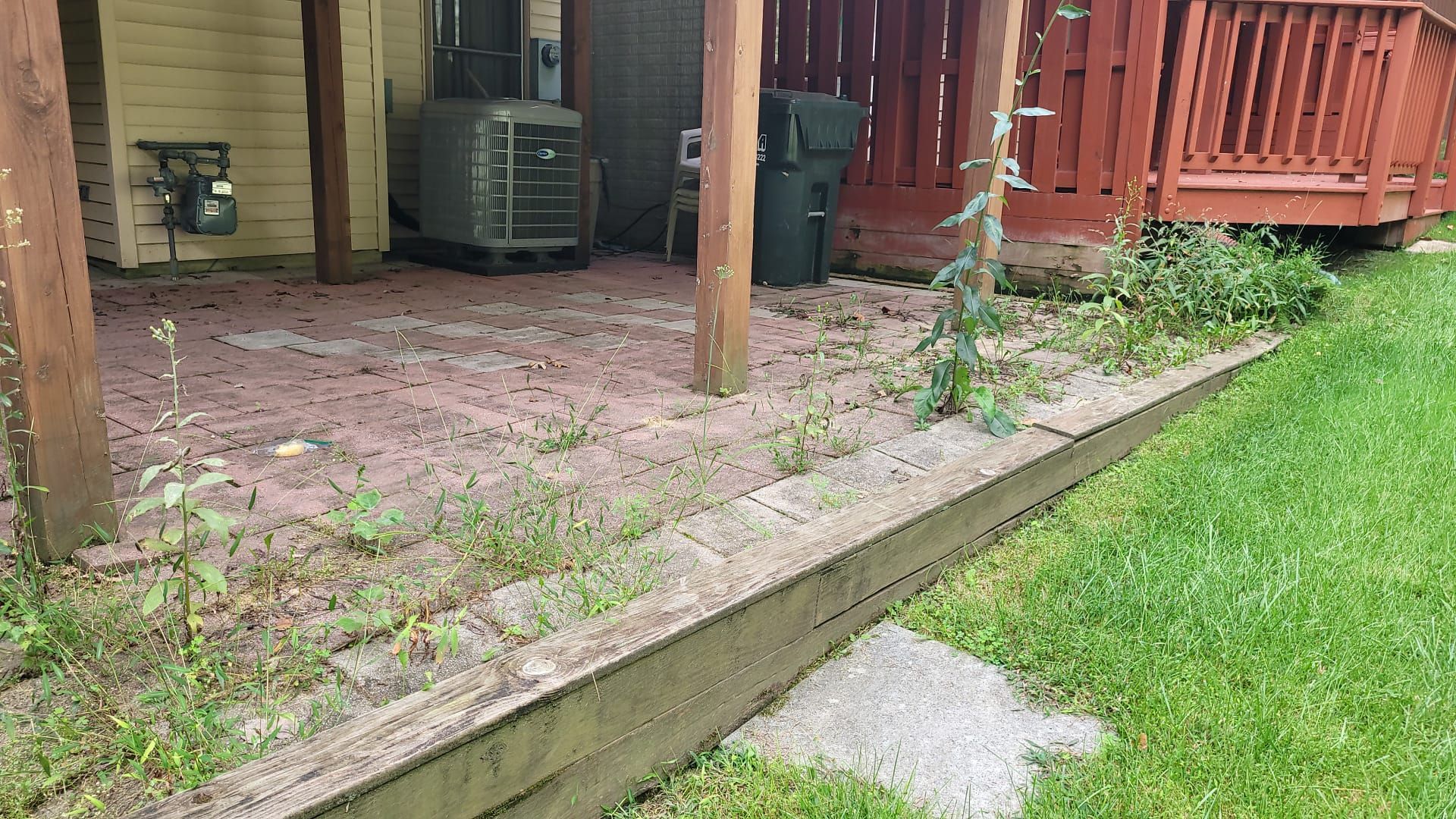 A patio with a red railing and a green trash can in the backyard of a house.