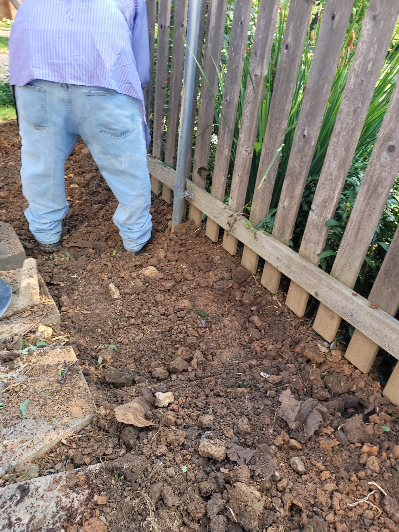 A person is standing in the dirt next to a wooden fence.