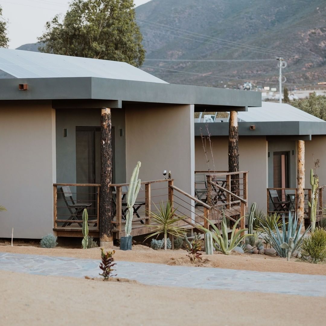 Fila de pequeñas cabañas beige con tejados oscuros y porches en un entorno montañoso rural
