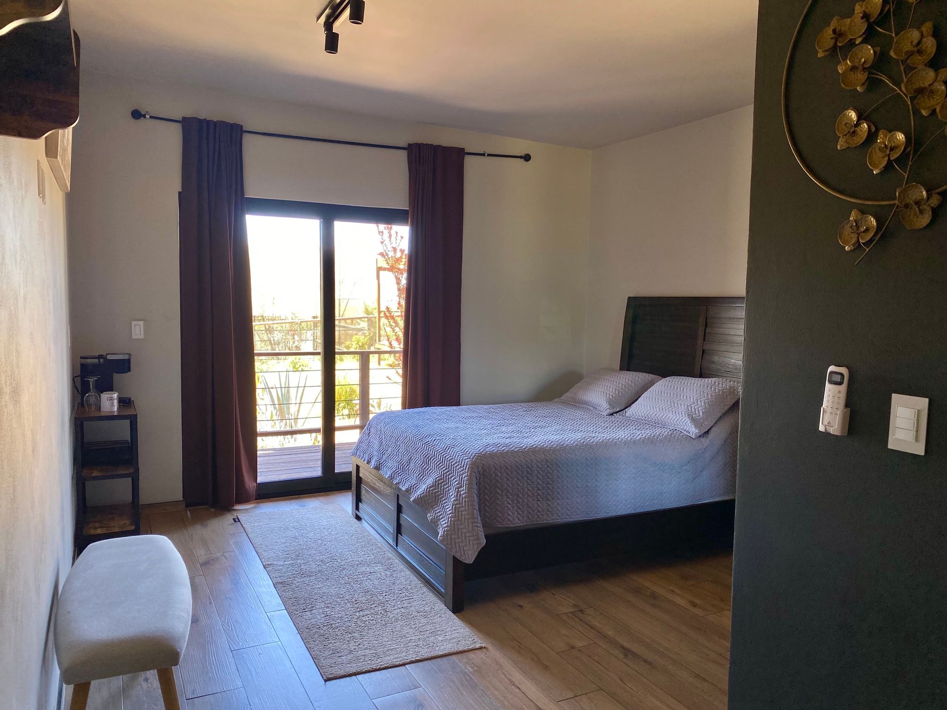 Dormitorio moderno con una cama, cortinas oscuras, un banco y puertas de balcón que dejan entrar la luz natural.