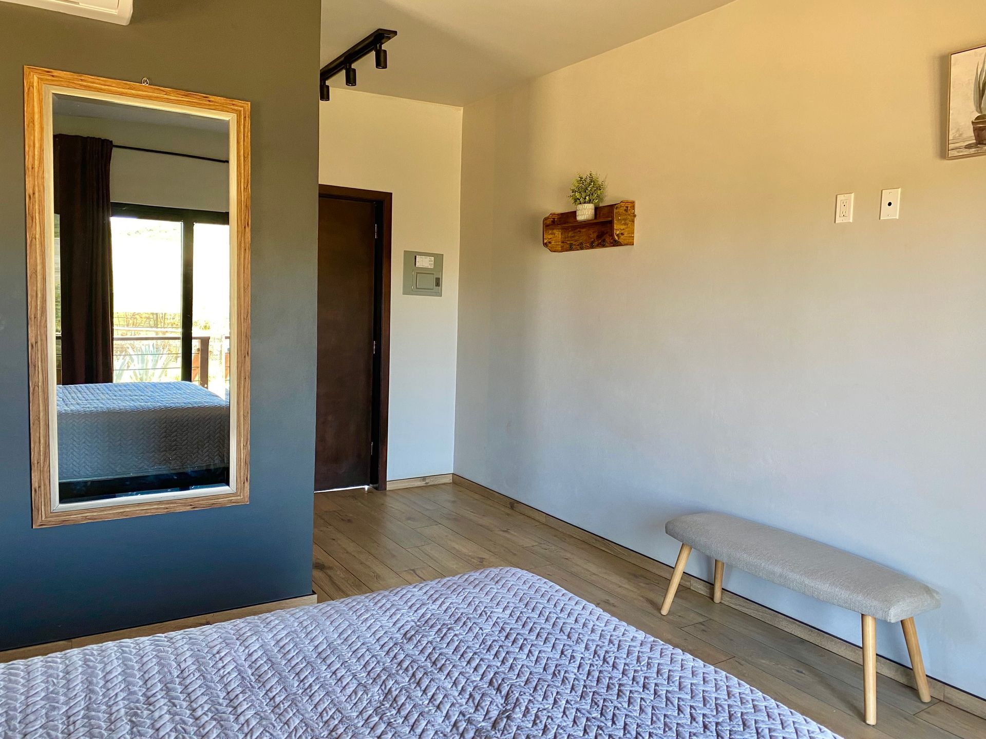 Dormitorio moderno con paredes grises, un espejo grande, cama, alfombra y un banco junto a la pared