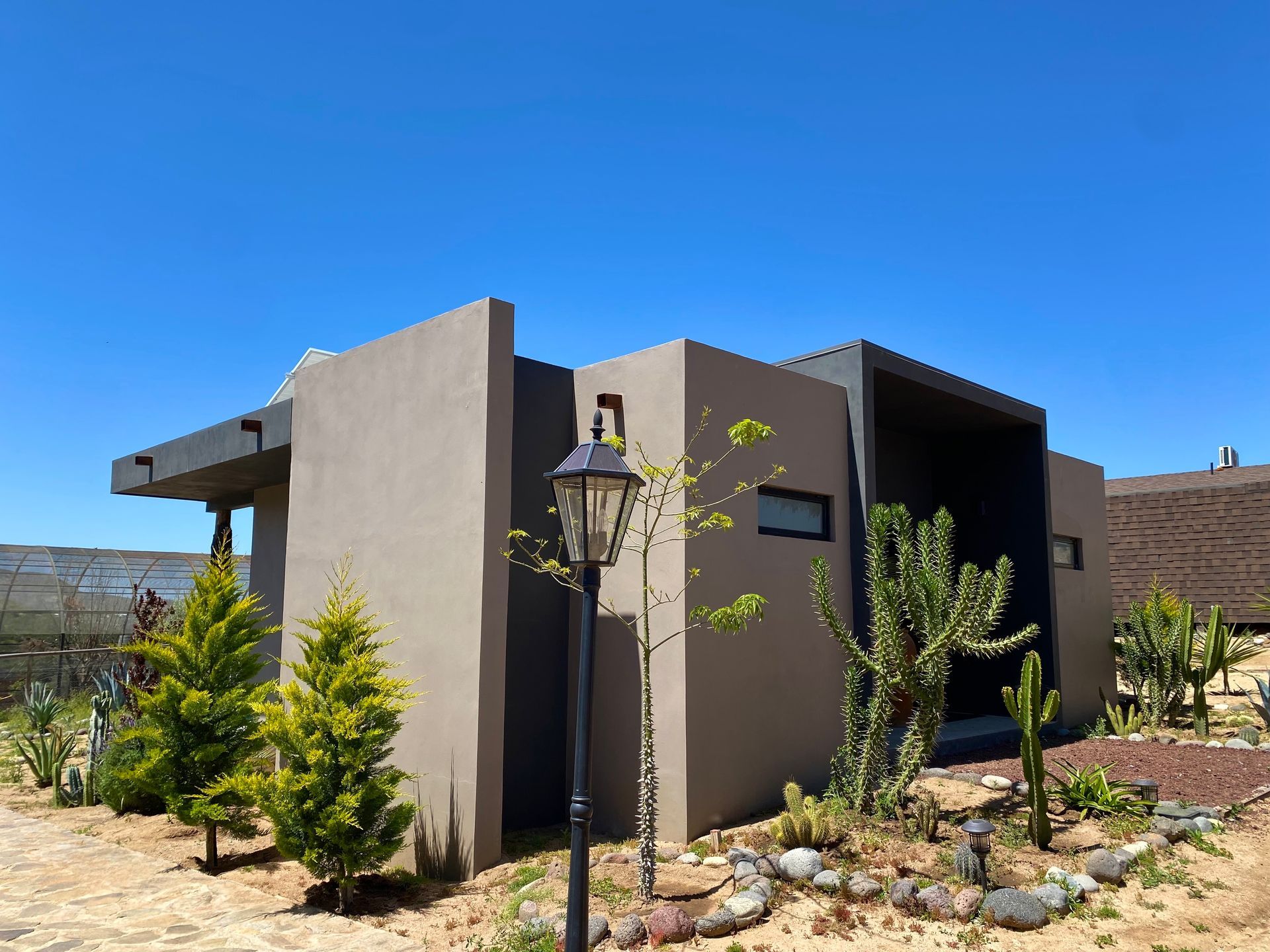 Casa moderna con paredes grises, techo plano y paisajismo desértico bajo un cielo azul despejado