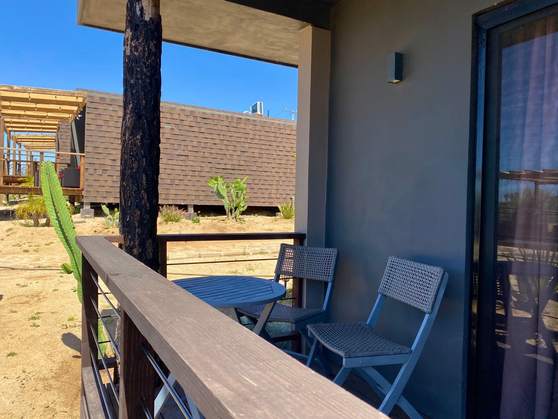 Pequeño patio a la sombra con dos sillas grises, una mesa de cristal y un jardín desértico al otro lado de la barandilla