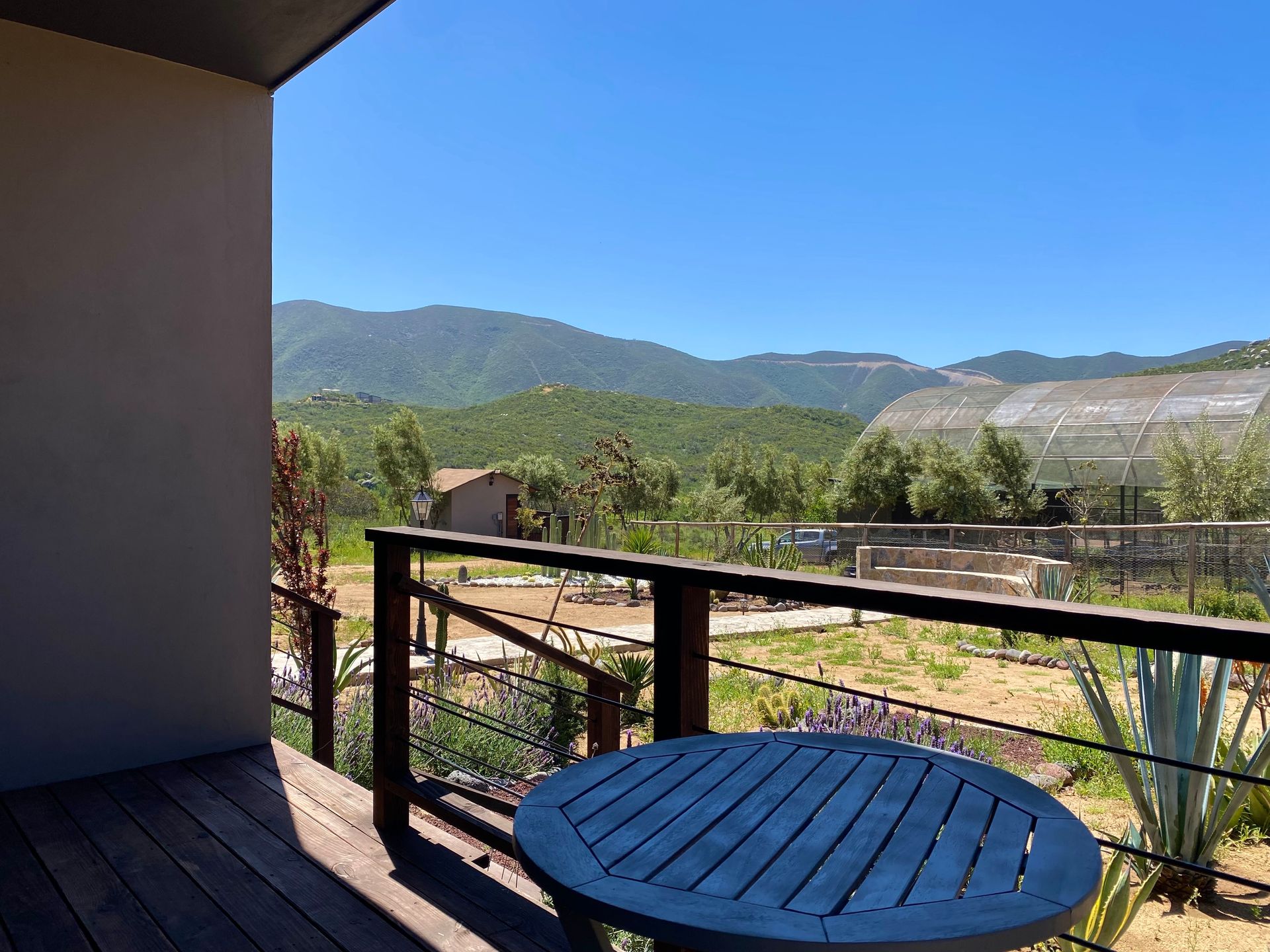 Patio cubierto con una mesa redonda desde la que se ven las montañas y un valle bañado por el sol