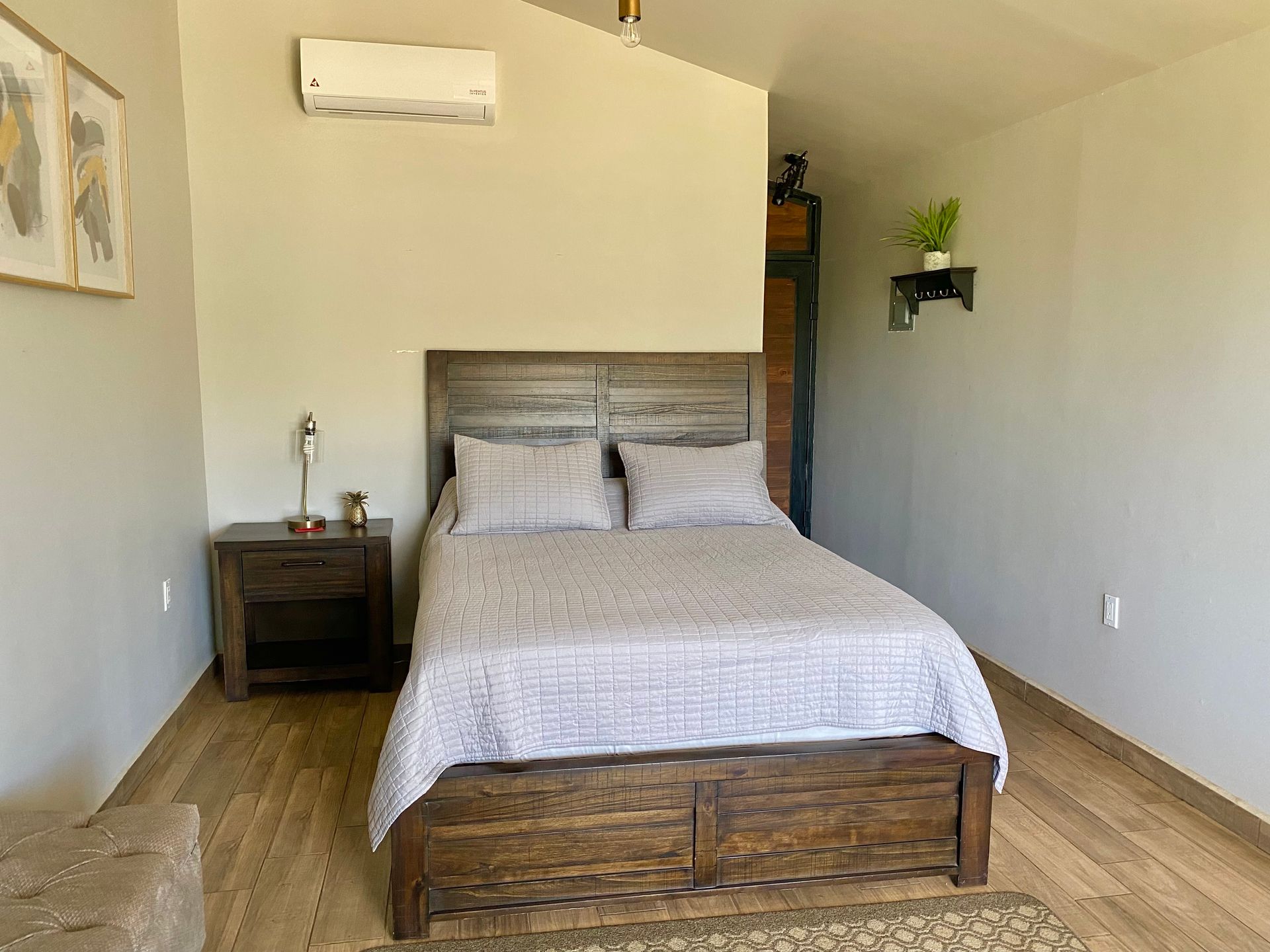 Dormitorio pequeño con una cama de madera, una mesita de noche, cuadros en la pared y paredes de color claro.
