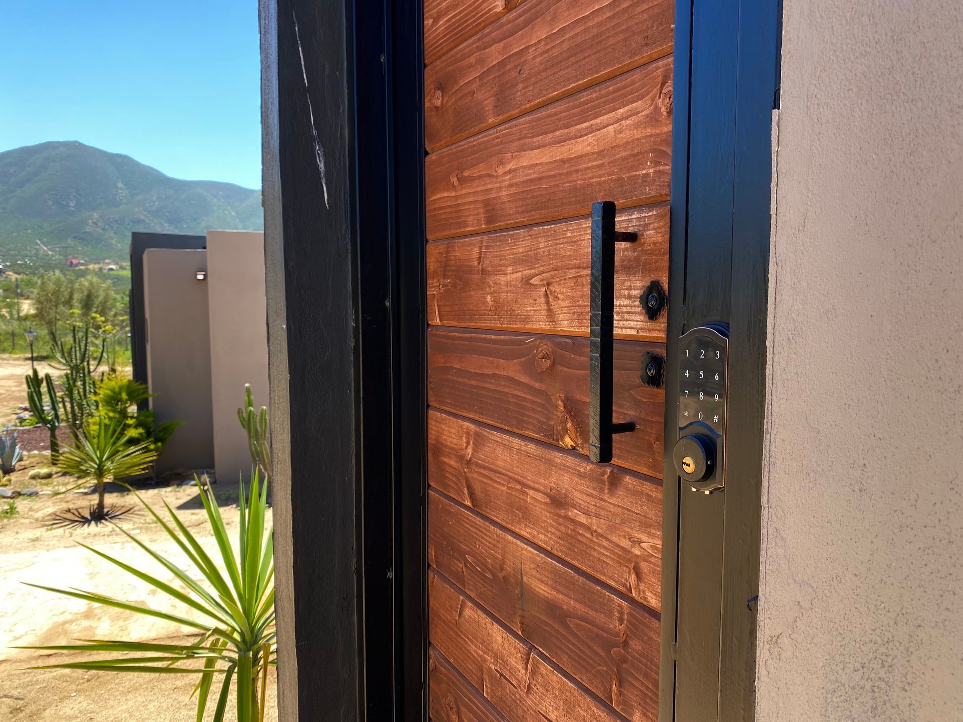 Puerta de entrada moderna con herrajes negros, junto a un patio y con vistas a las montañas del desierto