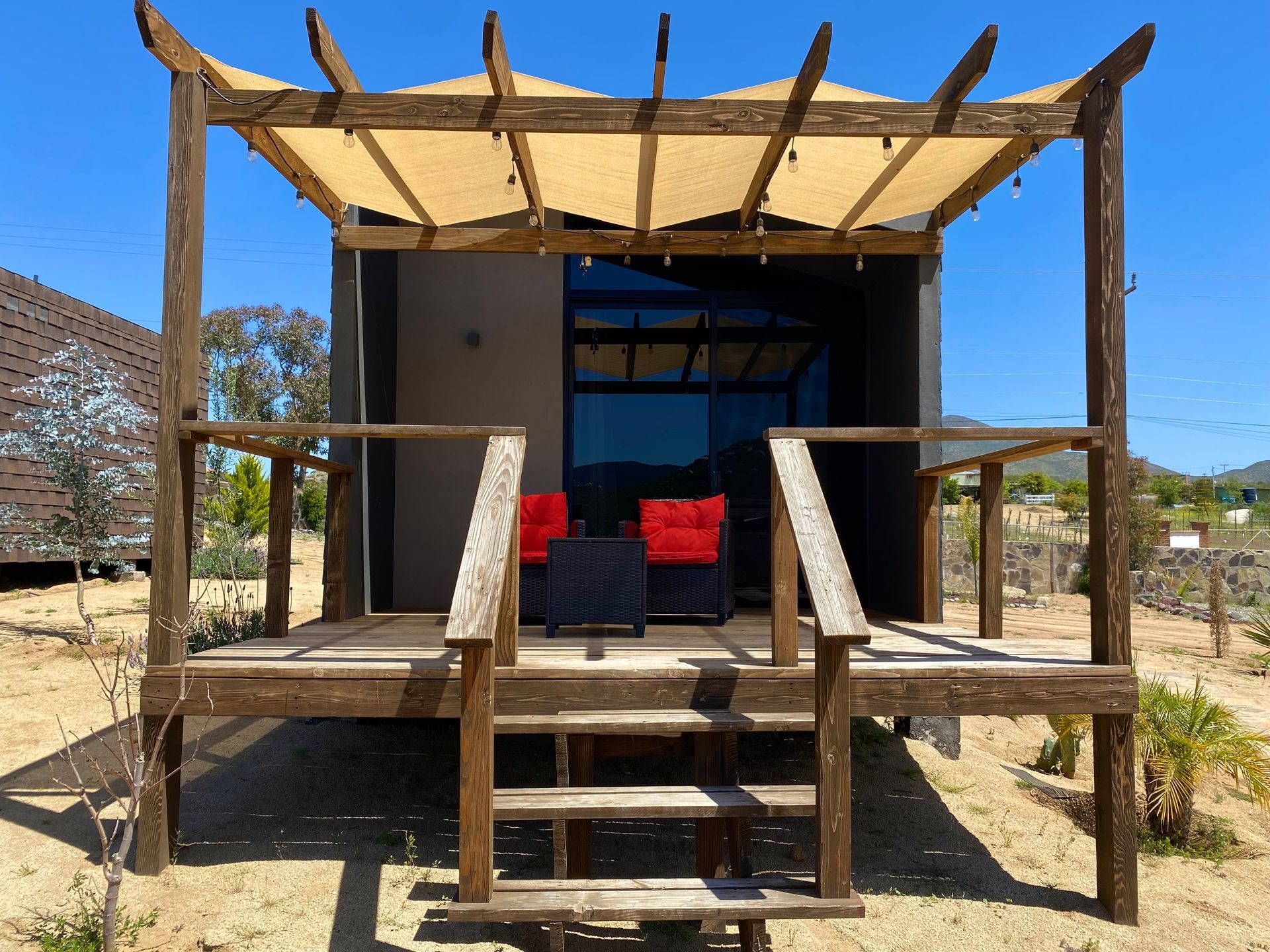 Pequeño porche de cabaña rústica con escalones, una silla roja y un toldo de lona en un entorno desértico