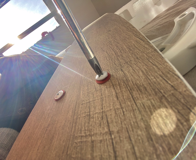 Screwdriver tightening a screw on a wood-grain surface. A white disc with a red ring is around the screw.