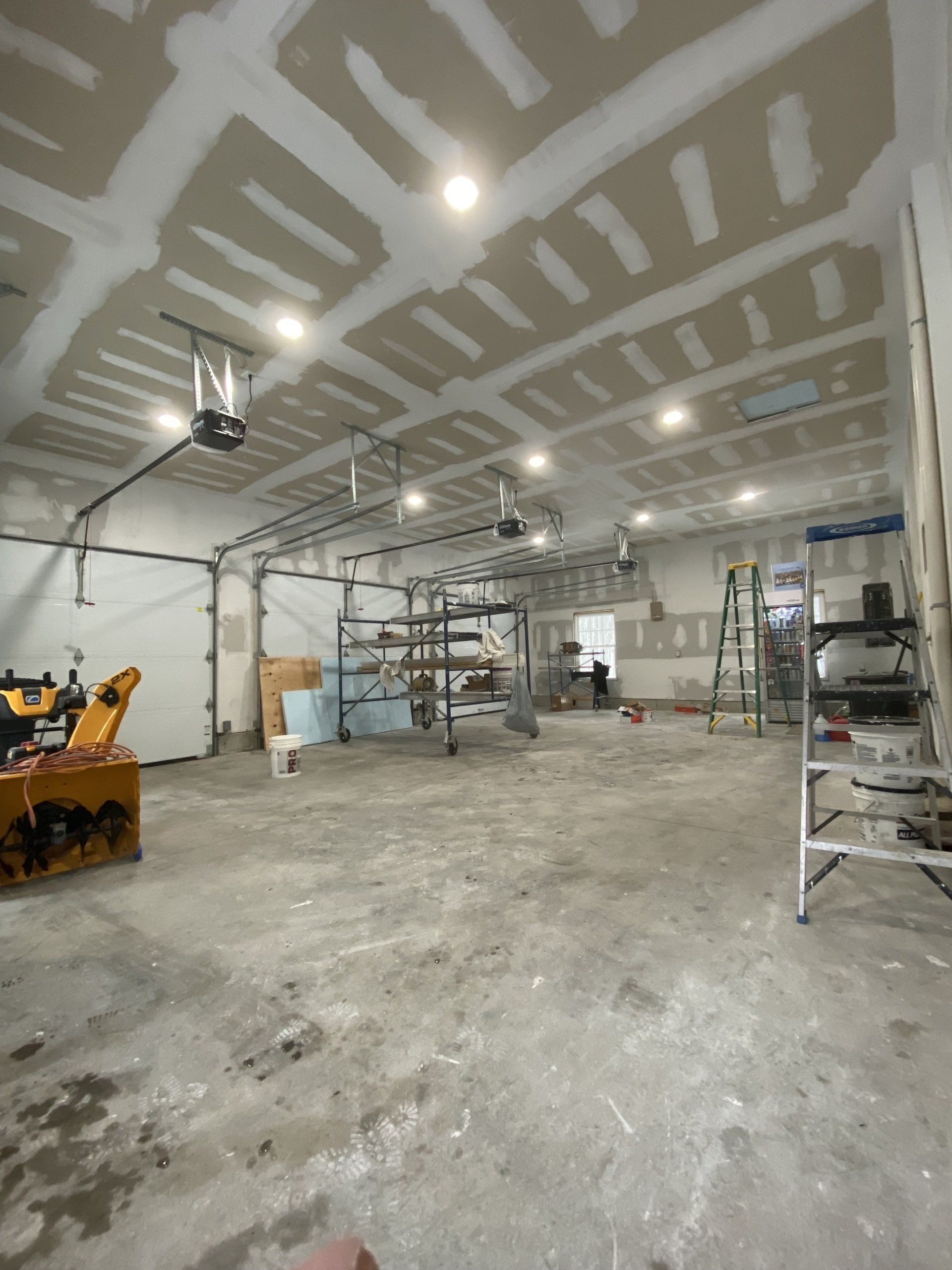 Garage interior under construction; drywall on ceiling and walls, various tools and equipment.