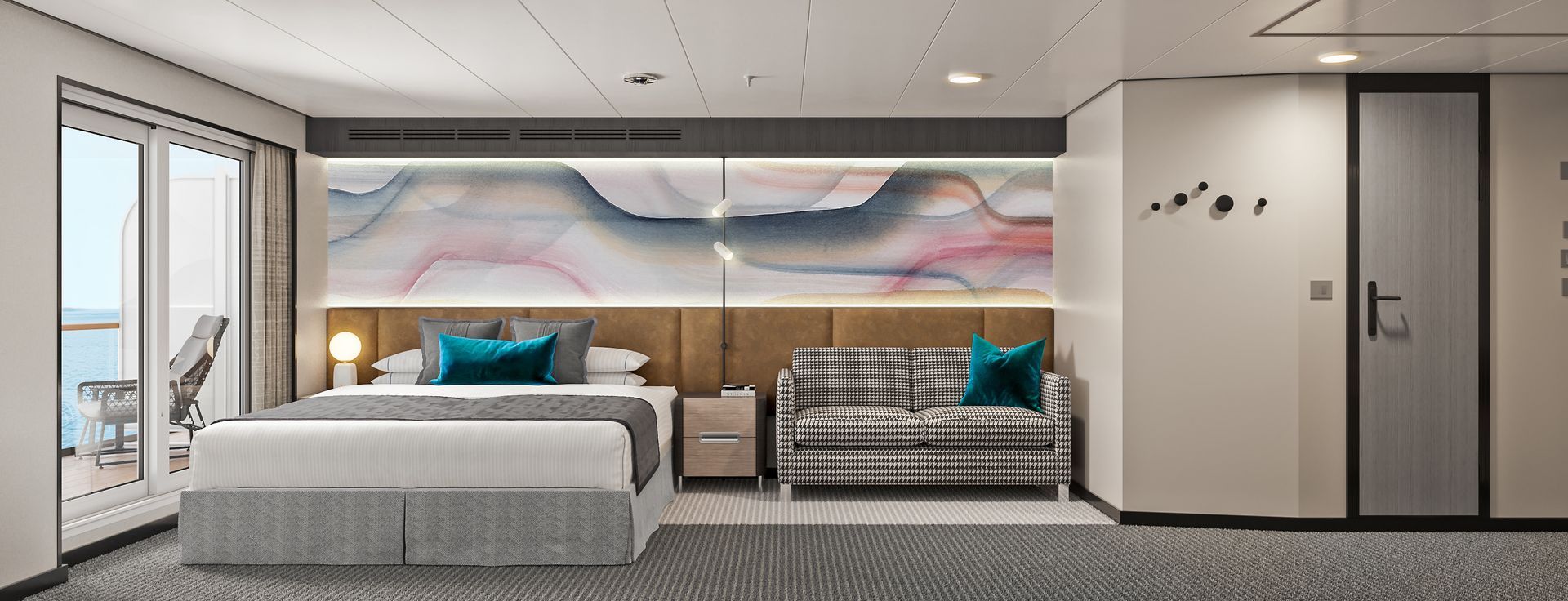A modern cruise ship cabin with a bed, a striped sofa, abstract wall art, and a balcony with outdoor seating.