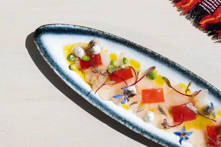 Long white platter with colorful garnishes and sauce, served on a light tablecloth