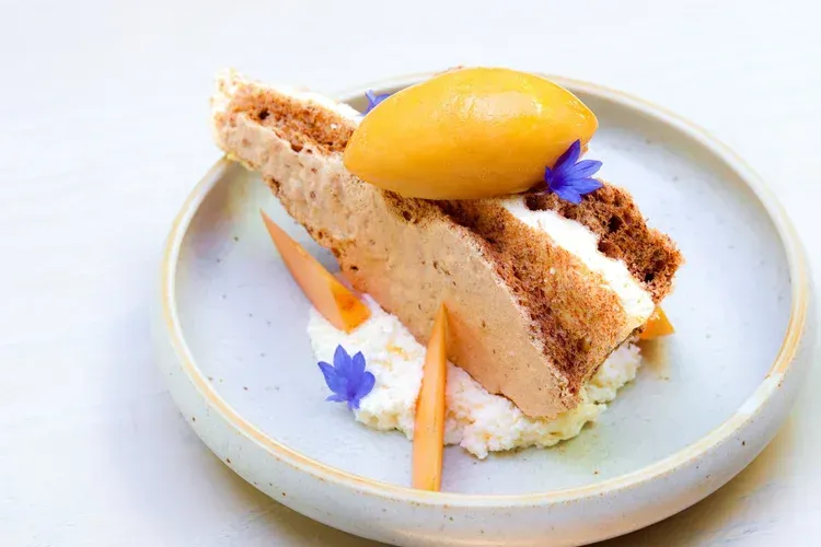 Dessert slice topped with mango sorbet and edible flowers on a pale blue plate