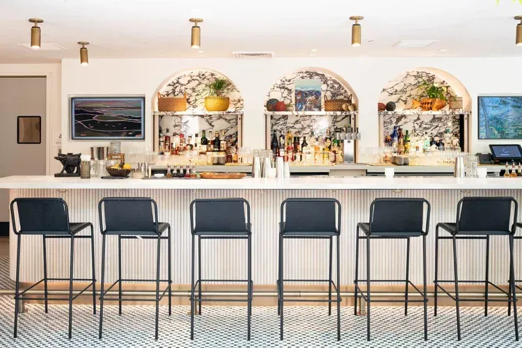 Bright modern bar with stools, patterned floor, arched shelves, and mounted TVs