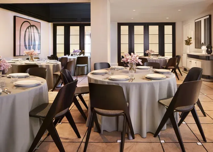 Elegant restaurant dining room with round tables, white tablecloths, dark chairs, and soft pink floral centerpieces