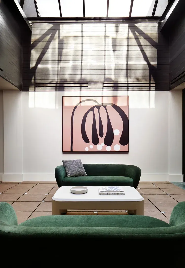 Modern lounge with green sofas, white coffee table, abstract wall art, and a glass skylight ceiling.
