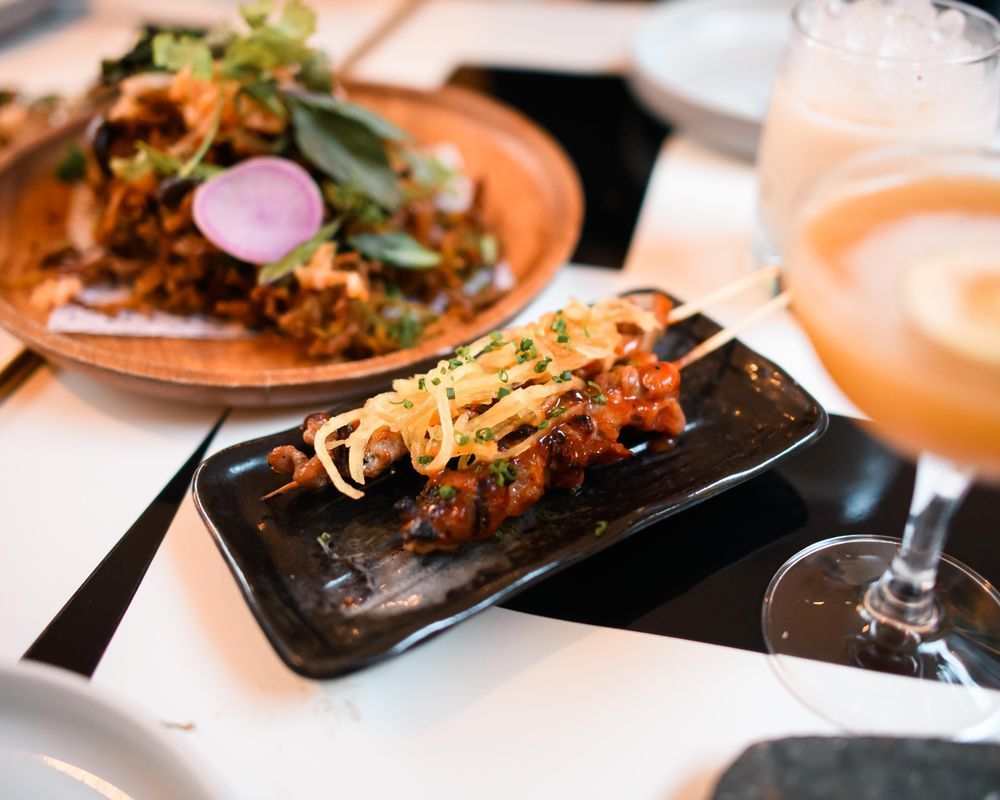 Plated gourmet dishes on a table, including a black rectangular plate and a glass of iced beverage