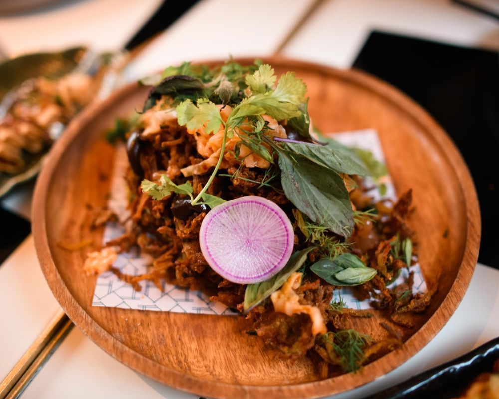 Wooden bowl of herb-topped shredded meat with a radish slice on a restaurant table