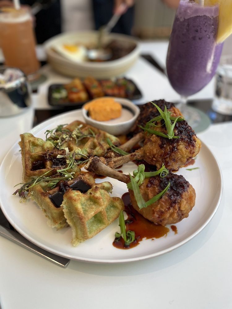 Plate of savory waffles and fried chicken with sauce, herbs, and a purple smoothie on a dining table