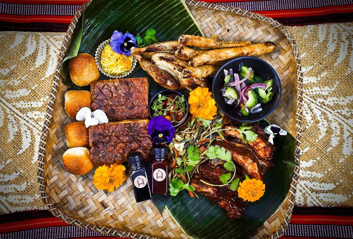 Assorted grilled foods and sides arranged on banana leaves over a woven mat