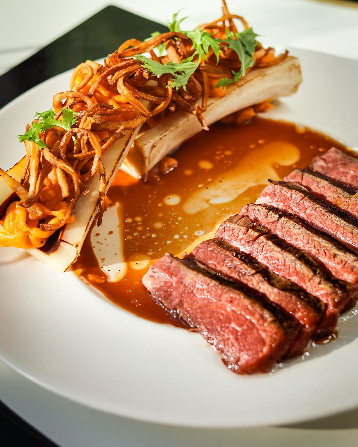 Sliced steak with sauce and fried onions on a white plate, garnished with herbs