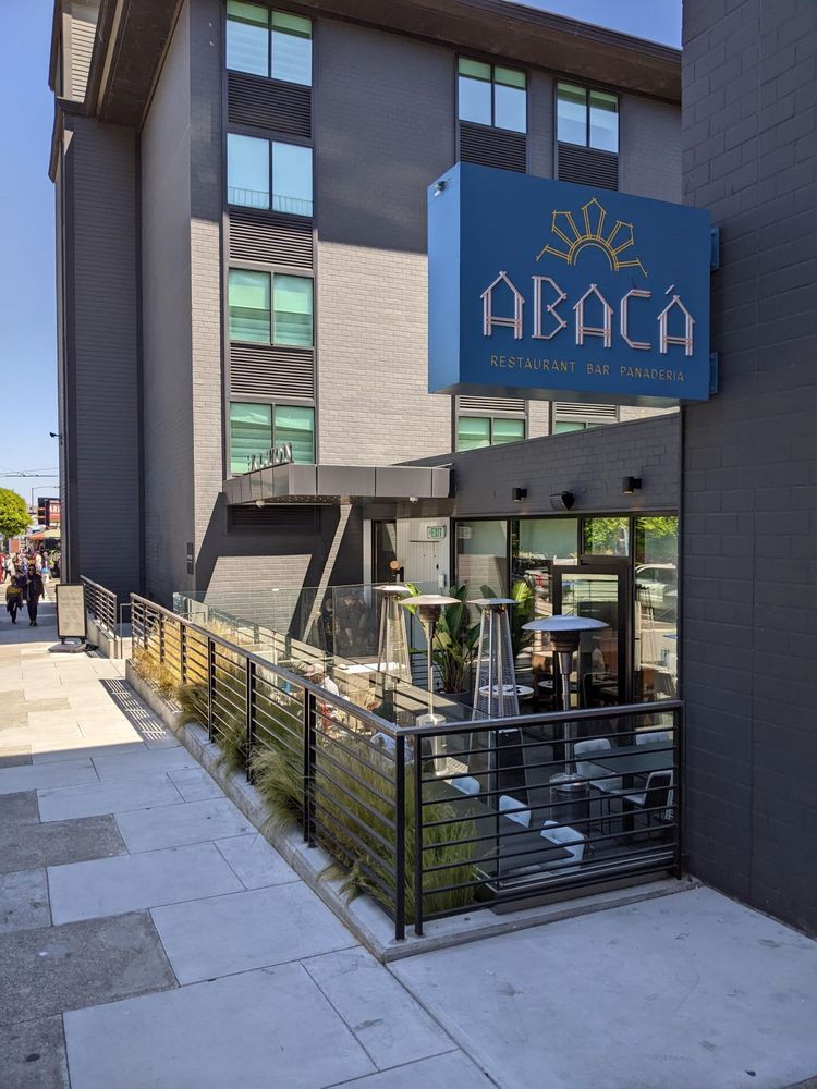 Exterior of ABACA café with blue sign and sidewalk patio seating beside a brick building