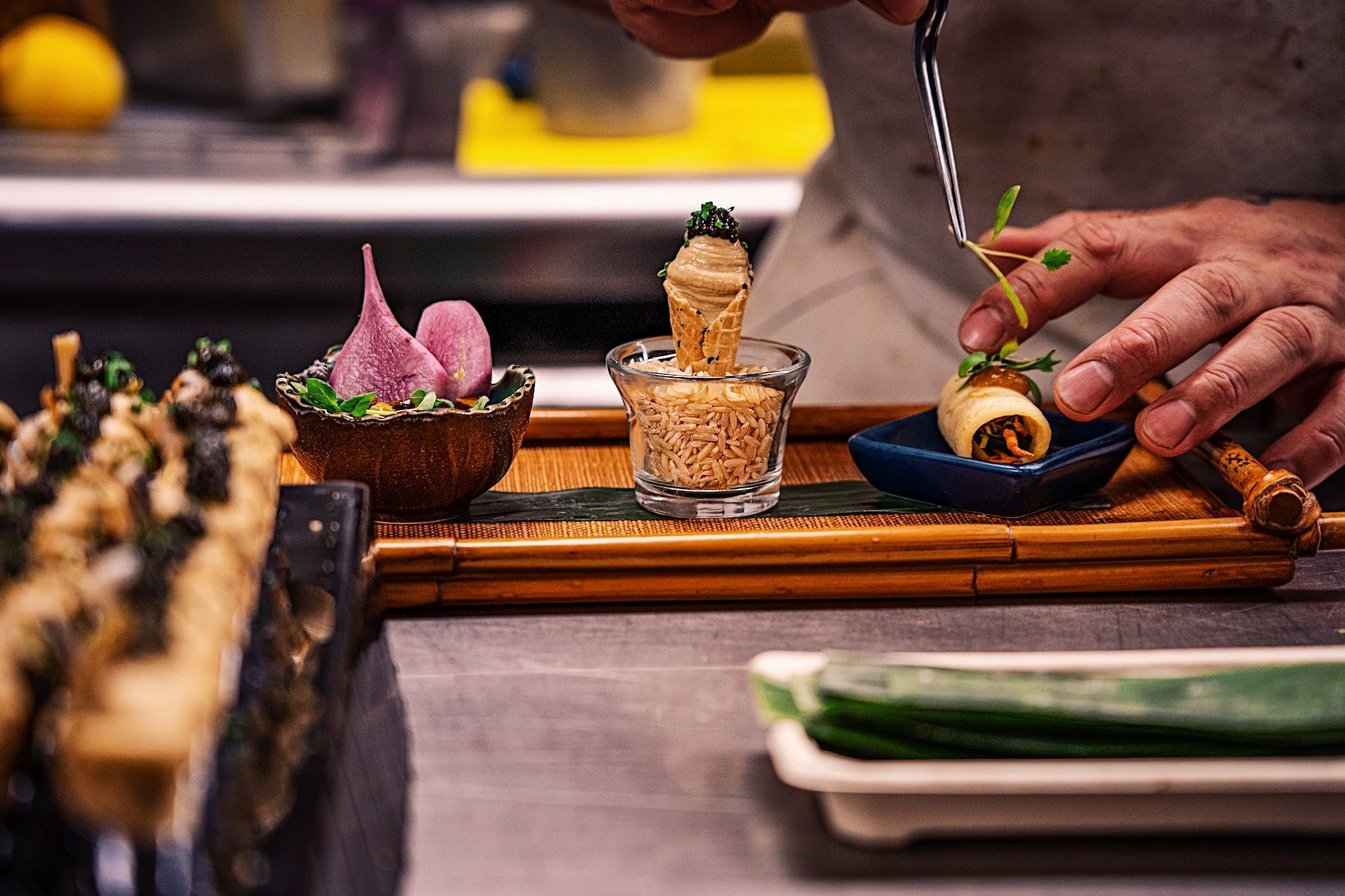 Hand arranging a gourmet dessert on a wooden tray with colorful garnishes and a small glass cup
