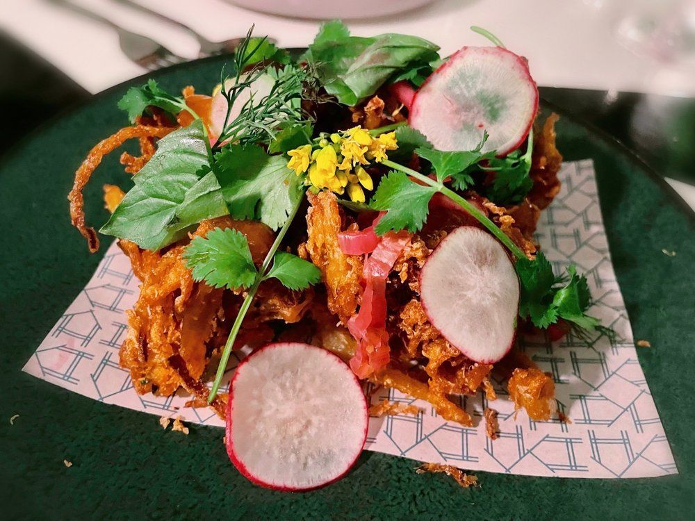 Gourmet plated dish with colorful vegetables, herbs, and sliced radishes on a patterned plate