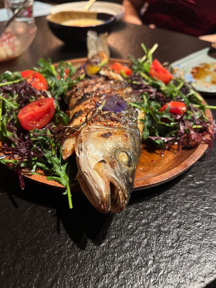 Grilled whole fish on a platter with greens and cherry tomatoes at a restaurant table