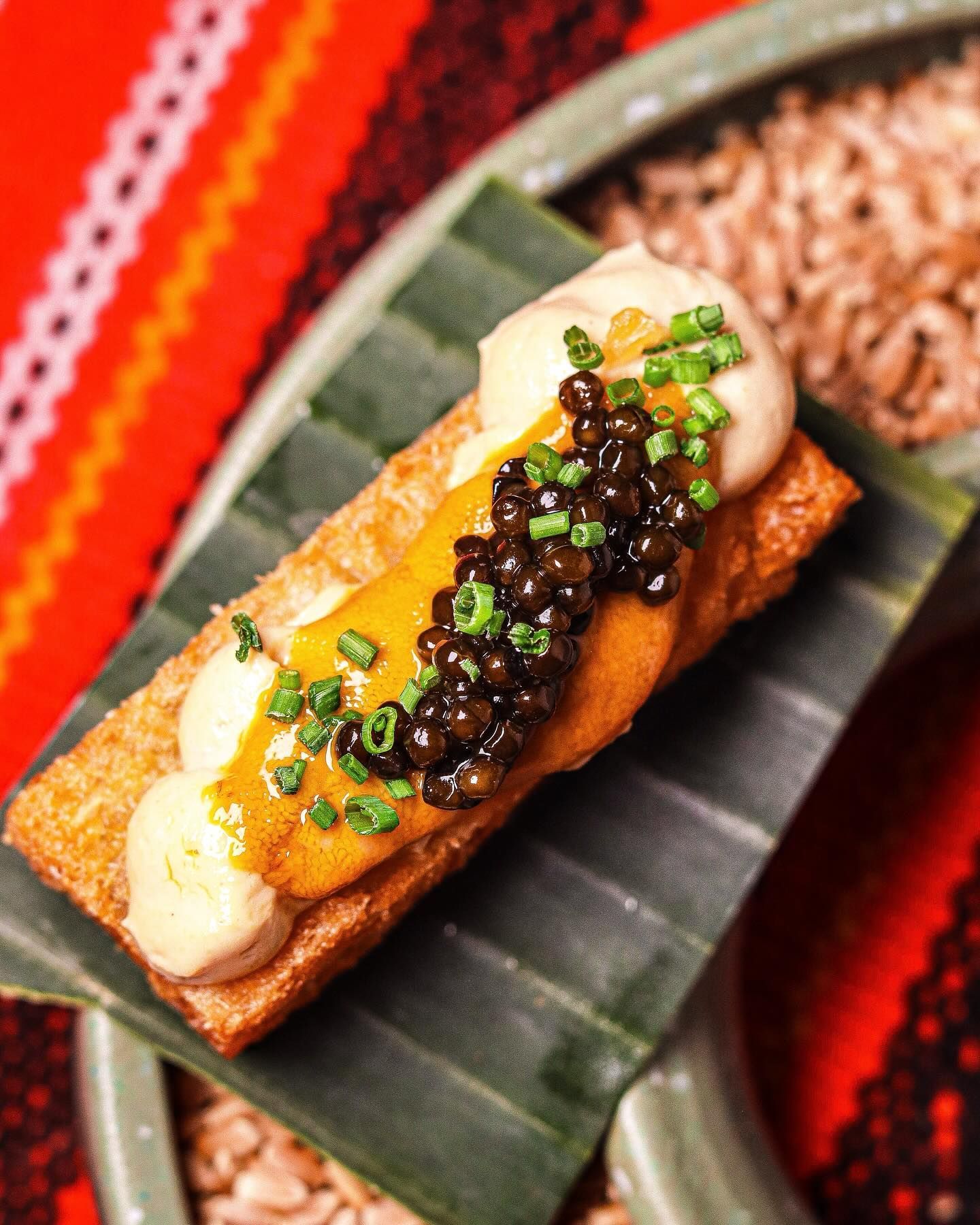 Gourmet canapé with caviar and cream on a banana leaf, set against a red woven background