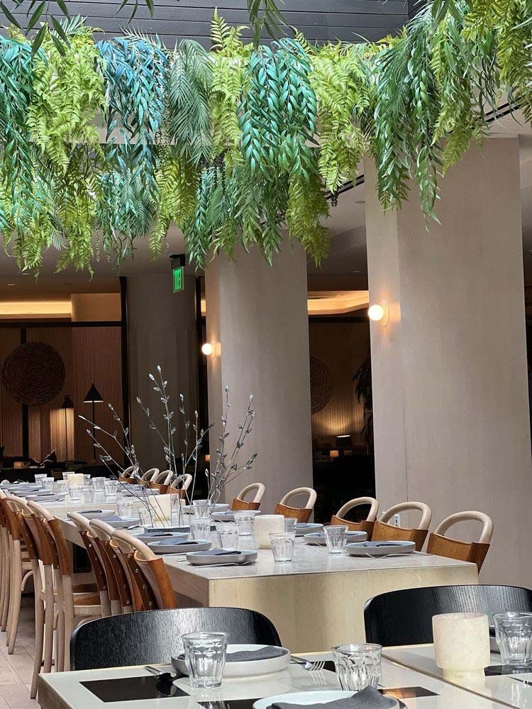 Elegant indoor dining setup with long tables, wooden chairs, and hanging greenery overhead