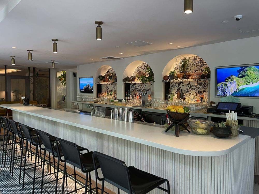 Modern hotel bar with white counter, black stools, floral wall niches, and two TVs.