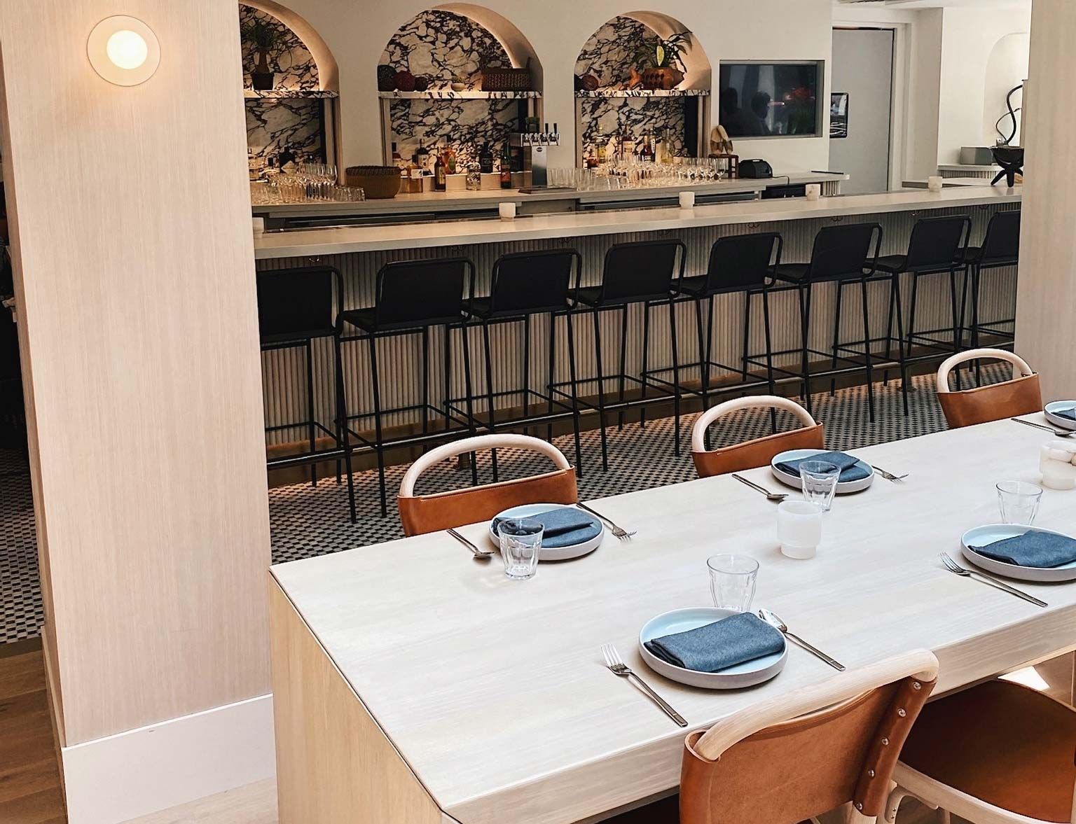 Modern dining room with a long white table, tan chairs, and a bar with black stools in the background