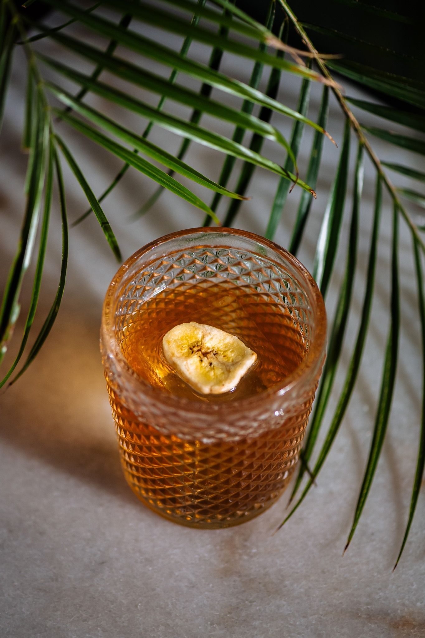 Orange drink in a textured glass with ice and lime, framed by palm leaves on a table
