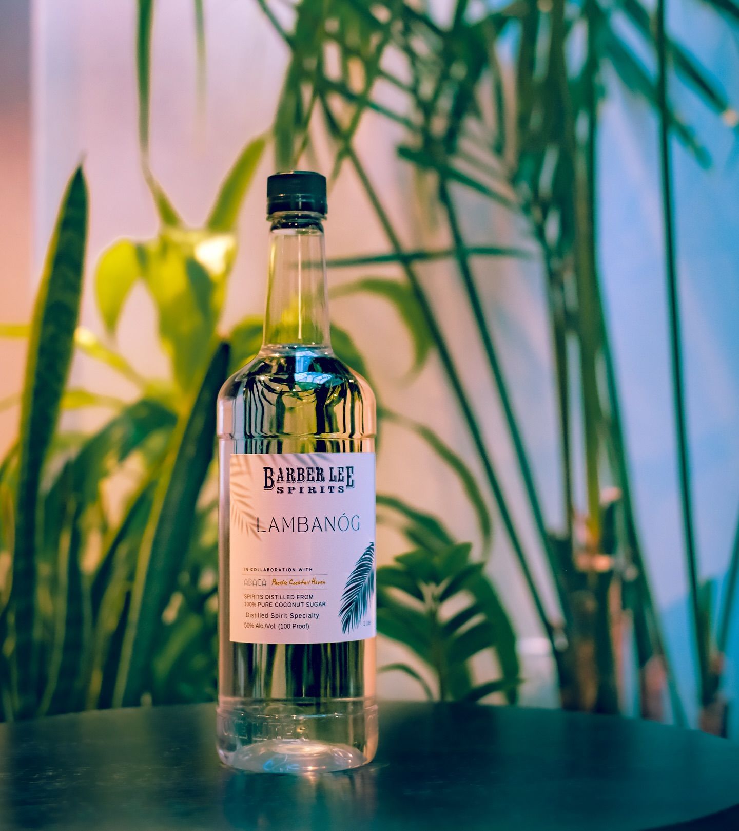 Clear bottle with a label on a table, against blurred green plants and colorful background.