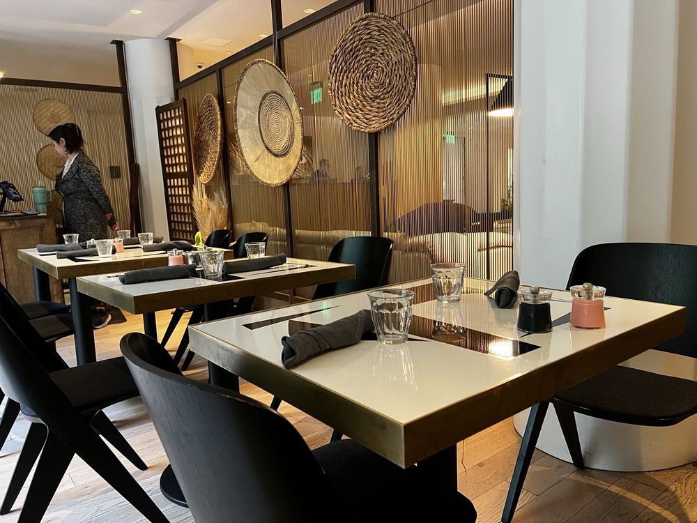 Modern restaurant dining room with white tables, black chairs, and woven wall decor