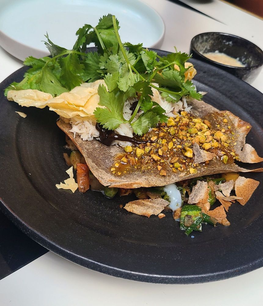 Grilled fish on a black plate with herbs, lemon, and sauce on a restaurant table